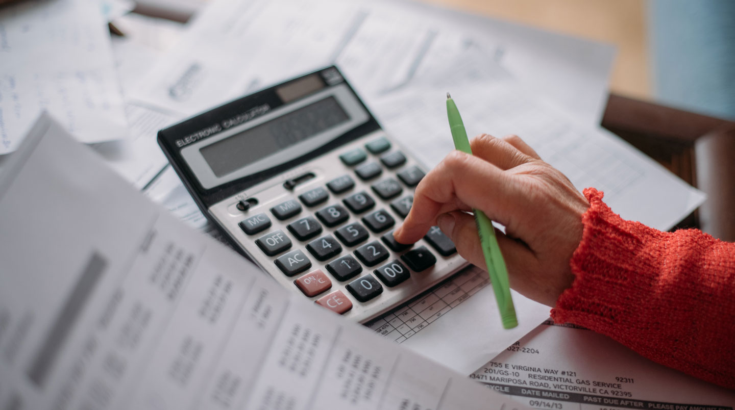 Gros plan sur une calculatrice moderne posée sur un bureau en bois clair avec des documents financiers floutés en arrière-plan